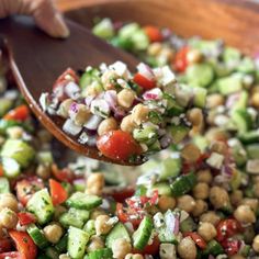 a wooden spoon full of salad with chickpeas, cucumbers and tomatoes