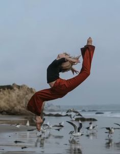 a woman doing a handstand on the beach with seagulls in the background