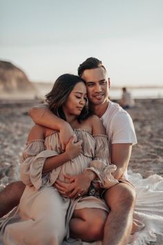 a man and woman are sitting on the beach hugging each other while they both have their arms around each other