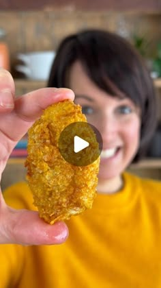 a woman holding up a fried food item in front of her face and smiling at the camera