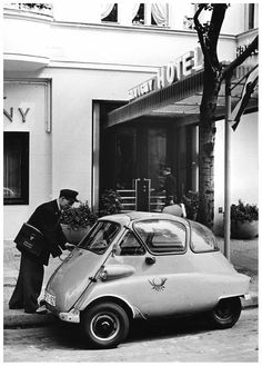 an old black and white photo of a man opening the door of a small car