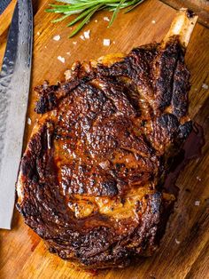 a piece of steak on a cutting board with a knife and rosemary sprig