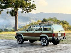 a brown and tan jeep parked on top of a wooden platform next to a tree