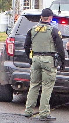 two police officers standing in front of a parked car on the side of the road