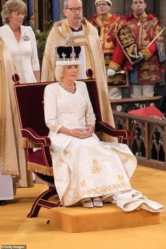 the queen is sitting on a chair in front of other people and wearing regal clothing