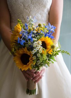 a bride holding a bouquet of sunflowers and daisies