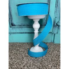 a blue ribbon wrapped around a white table lamp on carpeted floor next to wall