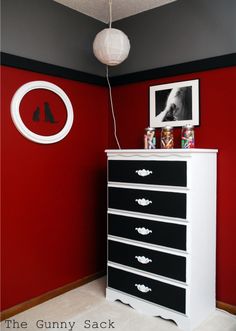 an empty room with red and black walls, white drawers and pictures on the wall