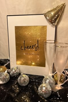 two champagne flutes and some disco balls on a table with a sign that says cheers