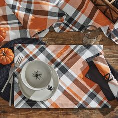 an orange and black table setting with spider napkins, silverware and pumpkins