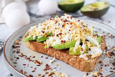 an open faced sandwich with avocado and other toppings on a white plate