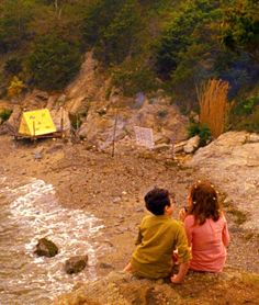 two children sitting on rocks near the water