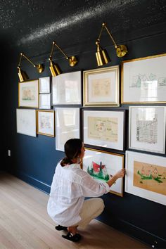 a woman kneeling down in front of a wall with pictures on it and hanging from the ceiling