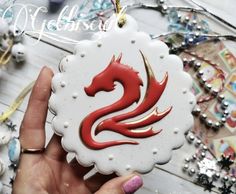 a hand holding a white ornament with a red dragon on it's side