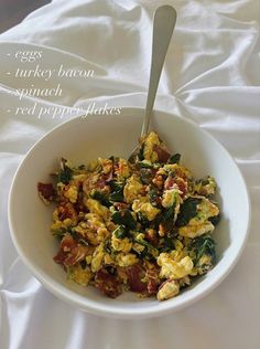 a white bowl filled with eggs and spinach on top of a white table cloth