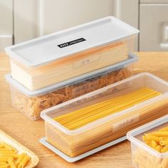 three plastic containers filled with pasta on top of a wooden table next to breadsticks