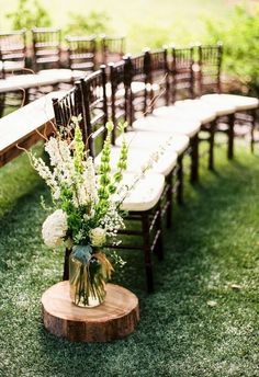 an arrangement of flowers and greenery sits on a wooden table in front of rows of chairs