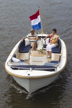 two people sitting on the back of a small boat with a flag flying in the background