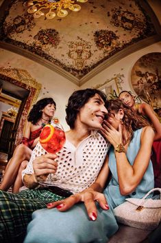 two women and one man are sitting on a couch with drinks in their hands as they look at each other