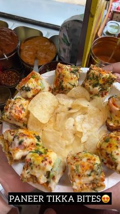 a person holding a plate full of food with chips and sauces on the side