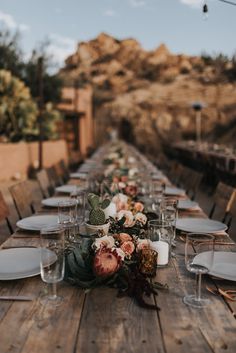 a long wooden table with white plates and flowers on it