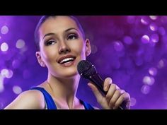 a woman holding a microphone in her right hand and smiling at the camera with purple lights behind her