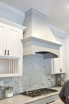 a man standing in front of a stove top oven under a white kitchen range hood