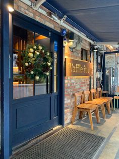 the outside of a restaurant with wooden chairs and wreaths on the front door window