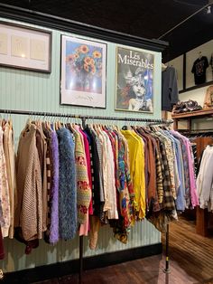 there is a rack full of clothes on the wall in this store with pictures hanging above it