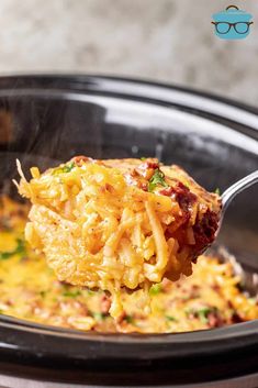 a spoon full of macaroni and cheese being lifted from the crock pot