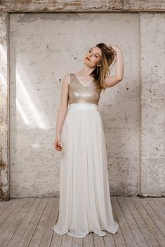 a woman in a white and gold dress posing for the camera with her hand on her head