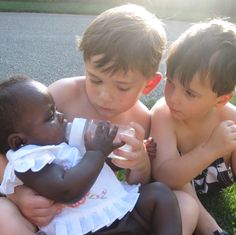 three children are sitting on the grass and one is holding a baby in his lap