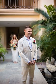 a man in a suit and tie standing next to a palm tree on the sidewalk