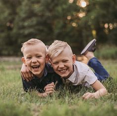 two young boys laying in the grass with their arms around each other and smiling at the camera