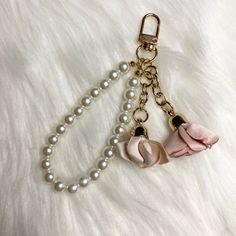 two pink flowers are attached to pearls on a white furnishing surface with a gold chain