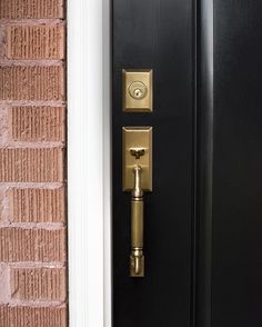 a black door with a gold handle on the side of it and a brick wall behind it