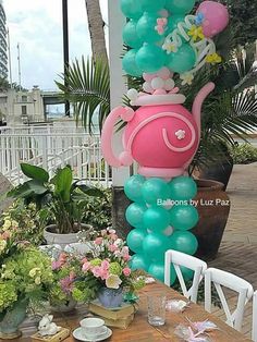 a table topped with balloons and flowers on top of a wooden table next to a potted plant