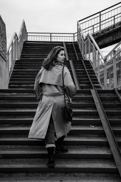 a woman walking up some stairs with a coat over her shoulders and handbag in her other hand