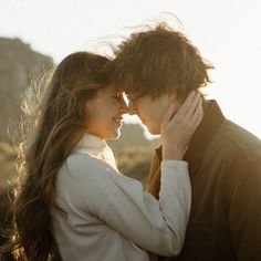 a man and woman standing next to each other in front of the ocean with their arms around each other