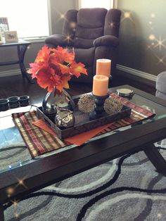 a living room with a glass coffee table and two chairs in the background, there is a candle on top of it