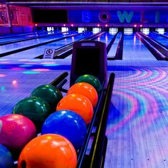 bowling balls are lined up in a row at the bowling alley with neon lights behind them