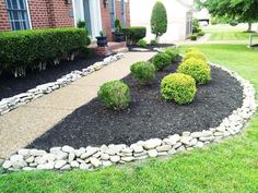 a rock garden bed in front of a brick house with green grass and bushes around it