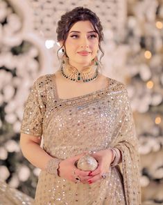 a woman in a gold dress holding a silver ball and wearing a necklace with pearls on it