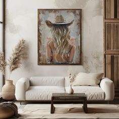 a living room with a white couch and a painting on the wall above it that has a woman wearing a cowboy hat