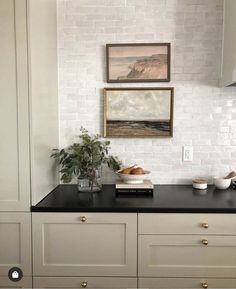 a kitchen with white cabinets and black counter tops is pictured in this image, there are two paintings on the wall