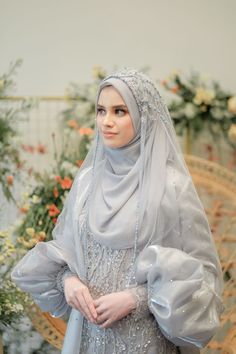 a woman wearing a gray dress and veil standing in front of some flowered bushes