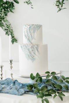 a three tiered white cake sitting on top of a table next to candles and greenery