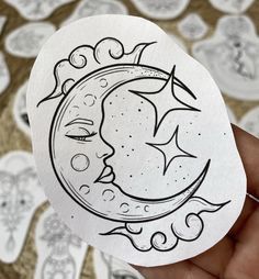 a hand holding up a sticker with the moon and stars on it in black ink