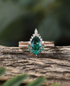 an emerald and diamond ring sitting on top of a piece of wood