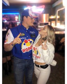 a man and woman standing next to each other in front of a bar with neon signs on the walls